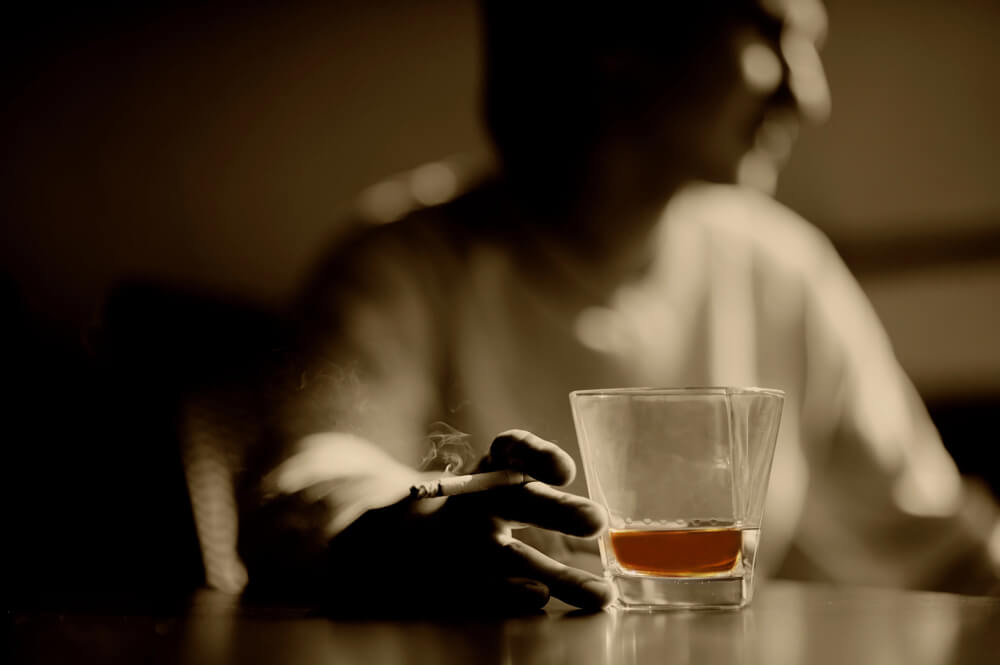blurred image of a person drinking whisky with a cigarette in his hand